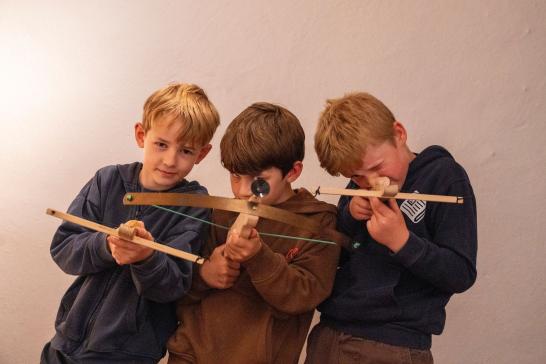 Drie jongens richten de speelgoed-kruisbogen van het museum op de camera